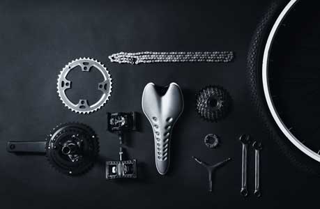 Collection of bicycle parts and accessories, featuring gears, pedals, tools, and bags, organized on a workbench for cycling maintenance and customization.