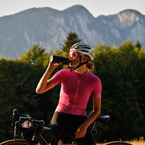 Woman riding her bicycle while drinking from a water bottle, staying hydrated during her ride.