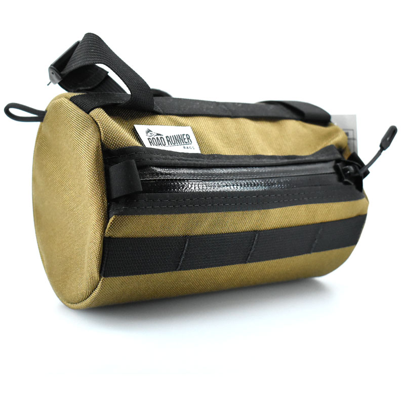 A photograph showcasing the Road Runner Bags Burrito Supreme bike handlebar bag. This compact, cylindrical bag is mounted on the handlebars of a bicycle, providing convenient and easily accessible storage for cyclists. The durable design, coupled with weather-resistant materials, ensures reliable protection for essentials such as snacks, gadgets, or small personal items during rides. The bag is securely fastened to the handlebars, offering a streamlined and stylish addition to the bike's accessories.