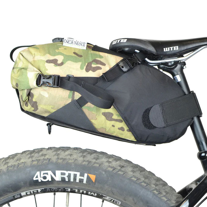A cyclist riding through a scenic mountain trail with the Oveja Negra Gearjammer Seat Bag mounted securely on the back of their bike, showcasing its functionality and durability.